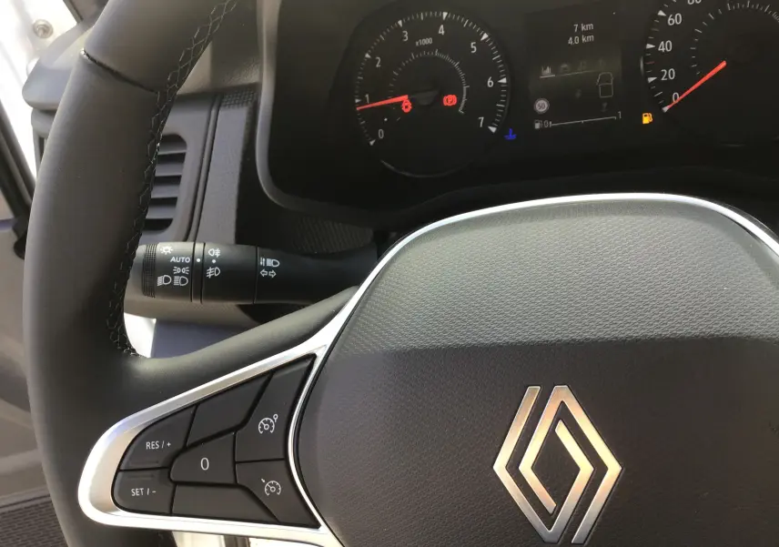 Gros plan sur le volant noir de Renault Trafic Fourgon blanc 2025 avec commandes au volant et tableau de bord partiel.