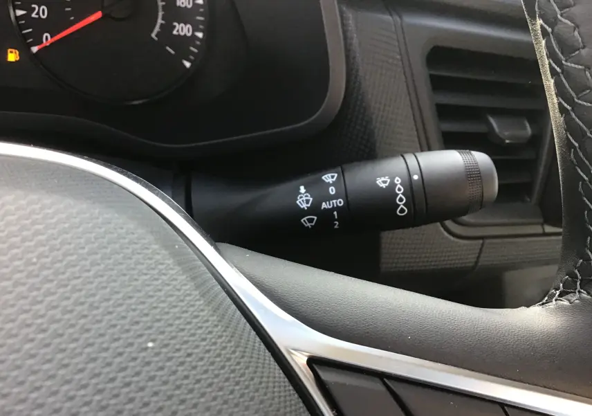 Gros plan sur la manette d’essuie-glace à droite du volant dans l’habitacle du Renault Trafic blanc, tableau de bord partiellement visible.
