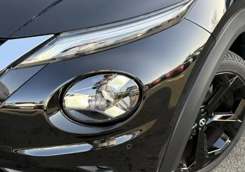 Gros plan sur le phare avant gauche et la jante noire du Nissan Juke 2024 Black Pearl, finition Tekna.