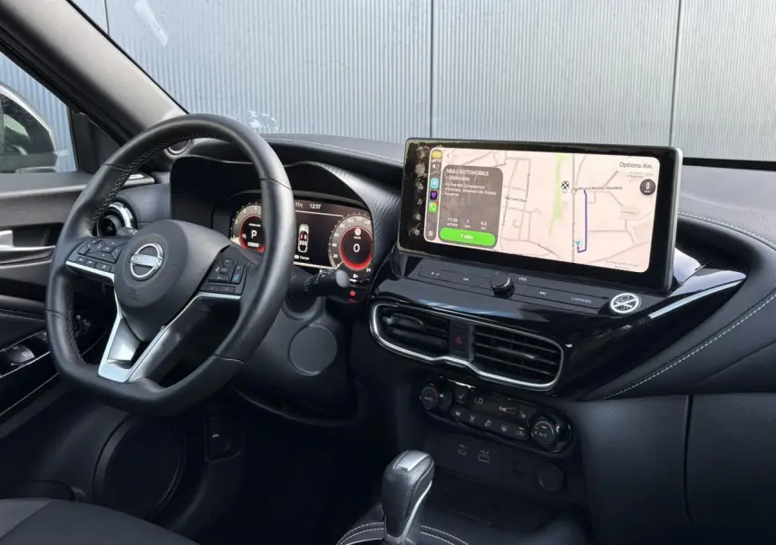 Vue intérieure côté conducteur du Nissan Juke 2024 avec tableau de bord noir et écran tactile affichant la navigation.