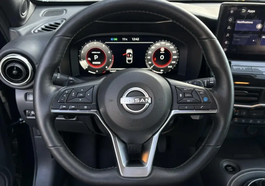 Vue rapprochée du volant noir du Nissan Juke 2024 avec commandes multifonctions et combiné digital lumineux.