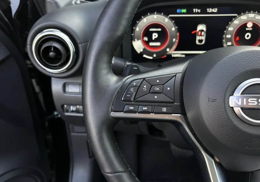 Gros plan sur le volant noir du Nissan Juke 2024 avec commandes intégrées et tableau de bord digital lumineux.