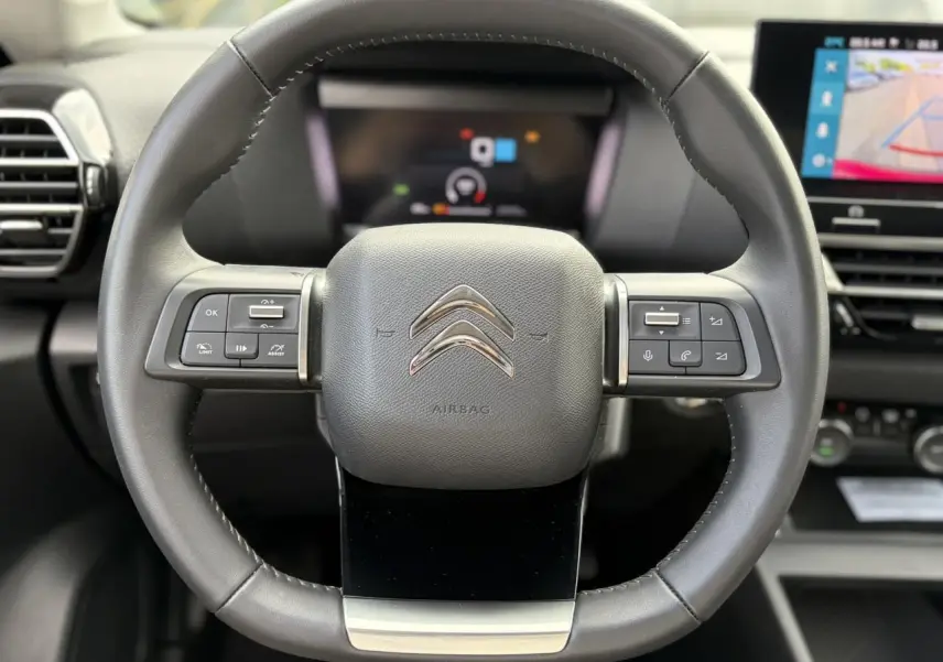Vue rapprochée du volant en cuir noir avec commandes intégrées et tableau de bord numérique d'une Citroën C4 2024.