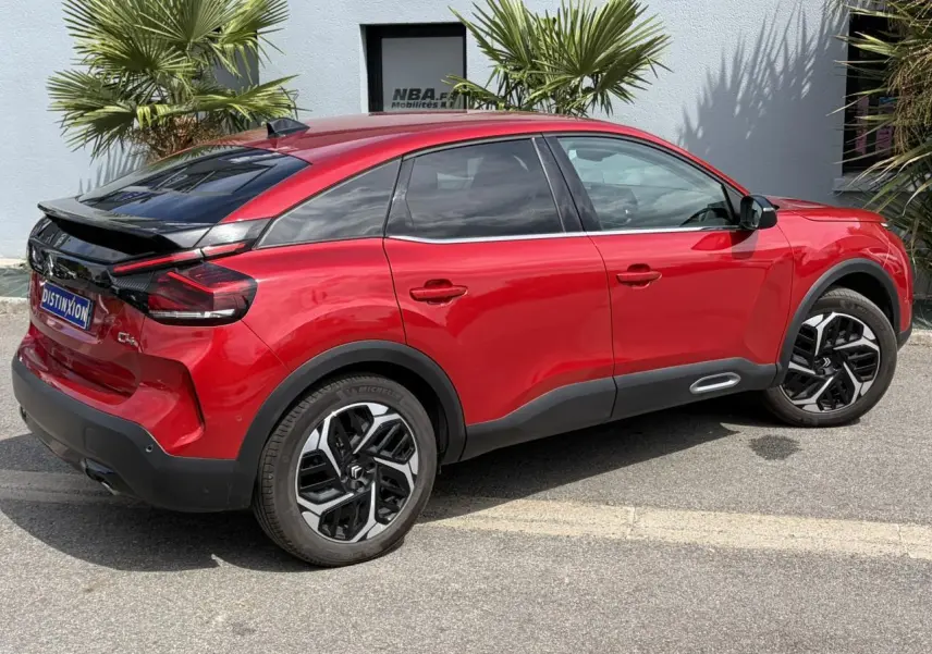 Vue 3/4 arrière droite d'une Citroën C4 2024 rouge Elixir avec jantes alliage noires et toit noir contrasté.