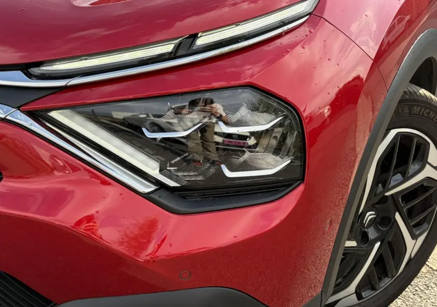 Gros plan sur le phare avant droit et la jante alliage noire et argent de la Citroën C4 Rouge Elixir 2024.