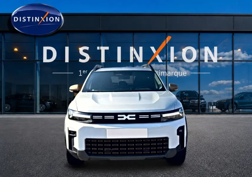 Vue avant d'un Dacia Bigster blanc avec calandre noire et logo DC, garé devant une vitrine Distinxion.