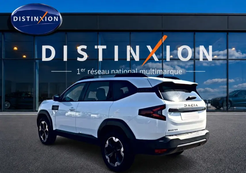 SUV Dacia Bigster blanc vu en 3/4 arrière droit, avec barres de toit et jantes alu noires.