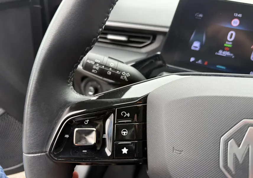Gros plan sur le volant noir du MG3 1.5 HYBRID+ 195 LUXURY avec commandes intégrées et tableau de bord numérique en arrière-plan.