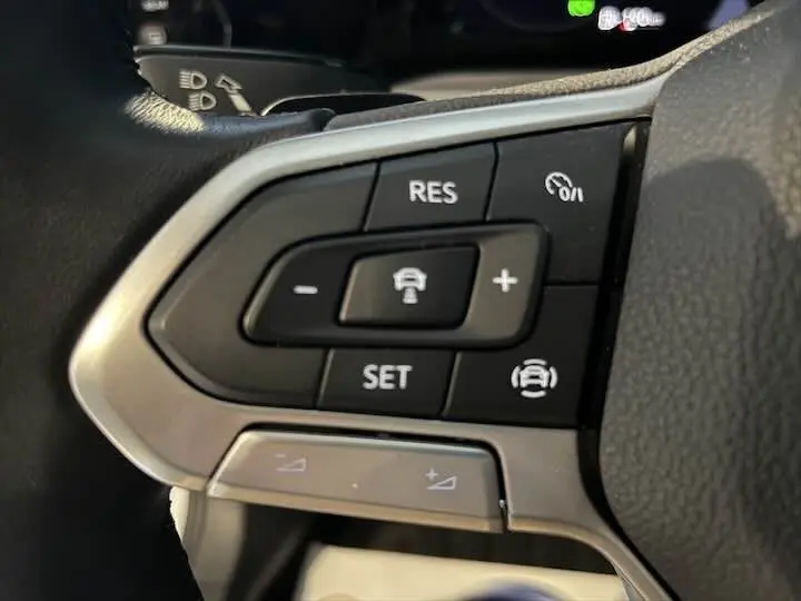 Gros plan sur les commandes du volant de la Volkswagen Golf 8 argentée, avec boutons de régulateur de vitesse et assistance conduite.