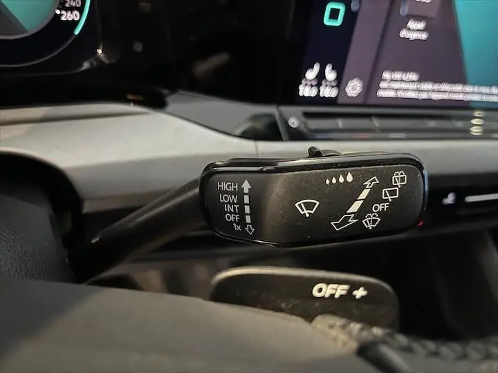 Gros plan sur le commodo d'essuie-glace noir dans l'habitacle d'une Volkswagen Golf 8 argentée, tableau de bord en arrière-plan.