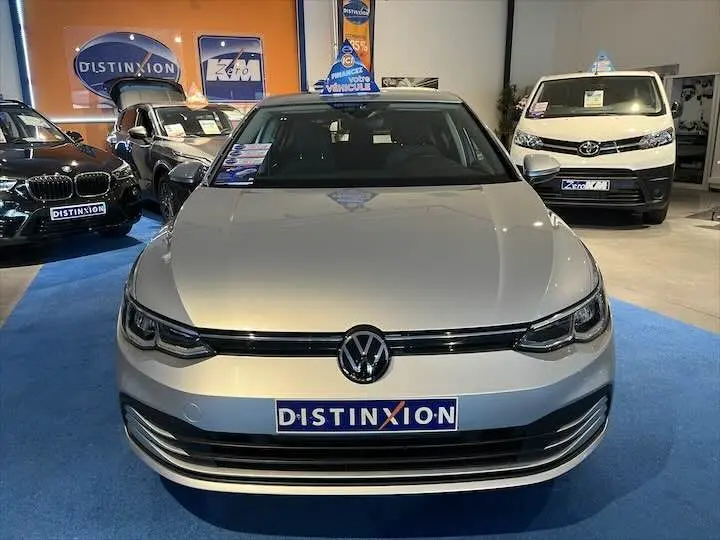 Vue frontale d'une Volkswagen Golf 8 argent métal exposée en showroom avec logo Distinxion visible sur la calandre.