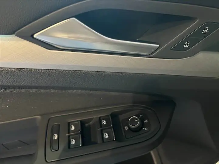 Gros plan sur la poignée de porte intérieure et les commandes électriques côté conducteur d'une Volkswagen Golf 8 argent métal.