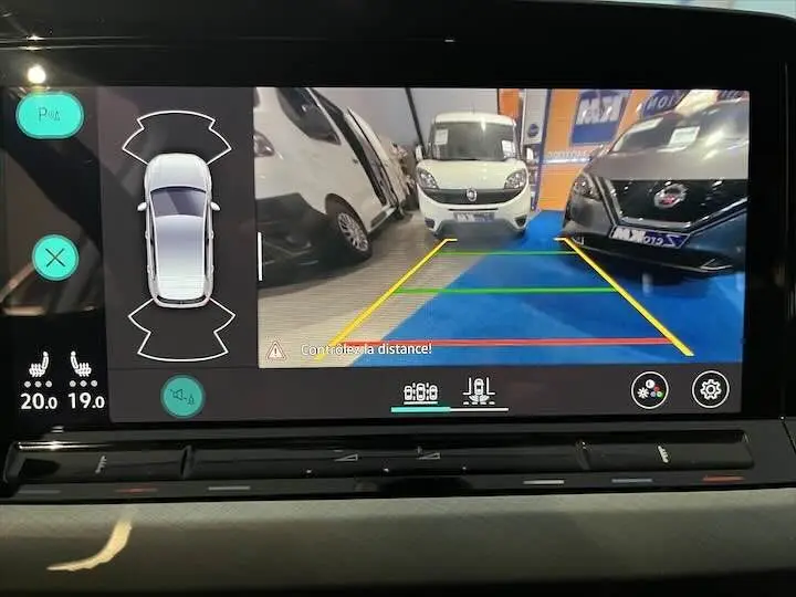 Vue caméra de recul montrant l'arrière d'une Volkswagen Golf 8 argent métal entre deux véhicules en intérieur showroom.