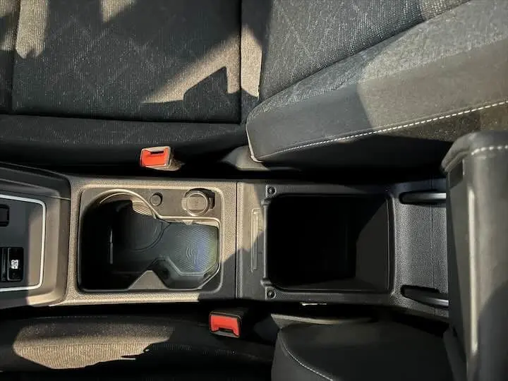Vue plongeante sur la console centrale noire de la Volkswagen Golf 8, avec porte-gobelets et accoudoir en tissu noir.