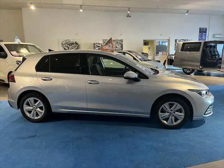 Profil côté gauche d'une Volkswagen Golf 8 argent métallisé exposée en intérieur sur sol bleu.