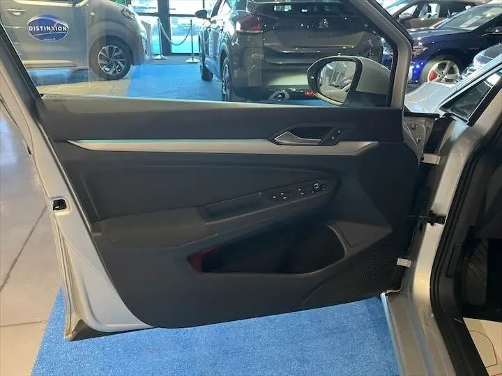 Vue intérieure de la porte avant gauche d'une Volkswagen Golf 8 argent métal, avec commandes électriques et garniture noire.