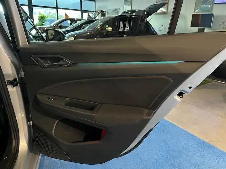 Vue intérieure de la porte côté gauche d'une Volkswagen Golf 8 argent métal avec éclairage d'ambiance bleu.