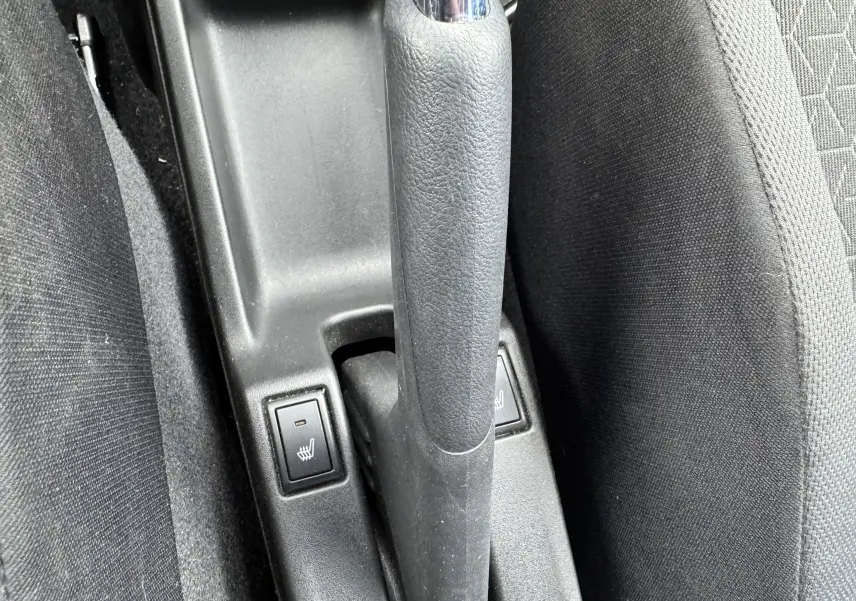 Vue rapprochée de la commande de frein à main et des boutons de sièges chauffants dans une Suzuki Swift bleu 2025.