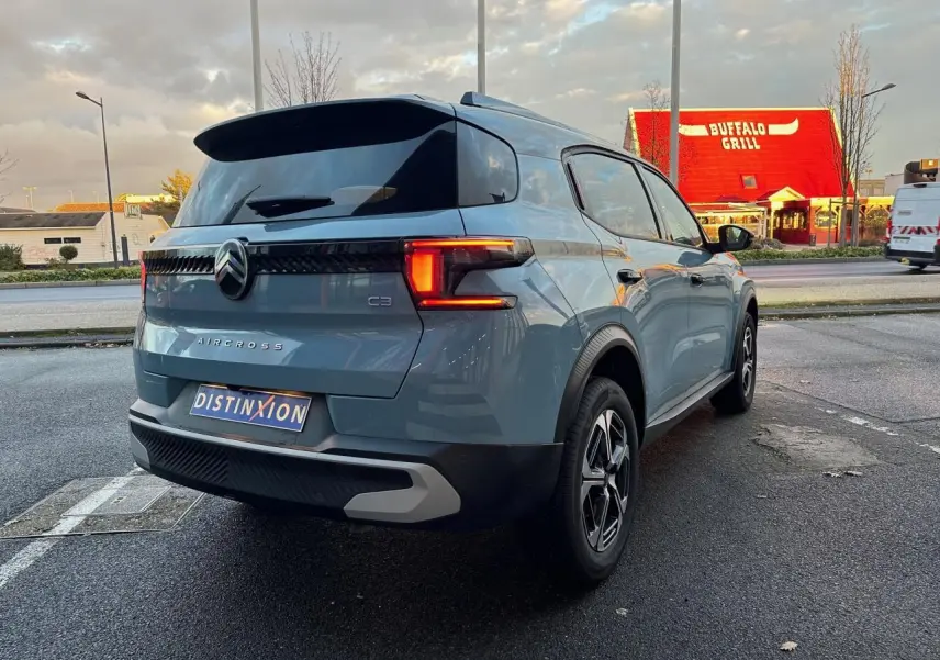 Vue 3/4 arrière droite d'une Citroën C3 Aircross bleu Monte Carlo avec toit noir et feux arrière LED allumés.