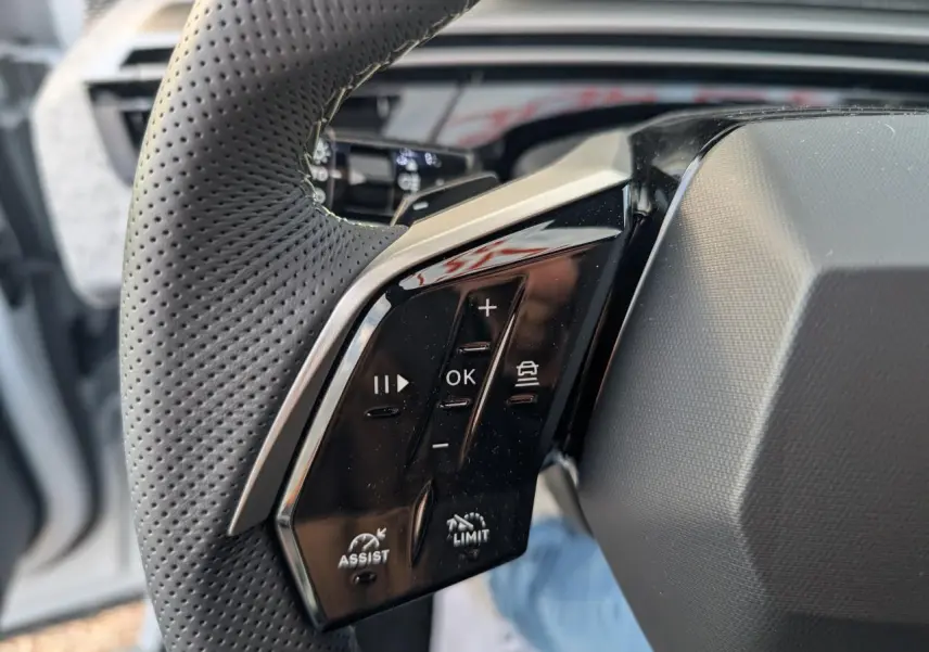 Gros plan sur les commandes gauche du volant perforé noir laqué du Peugeot 3008 blanc hybride 2025 GT