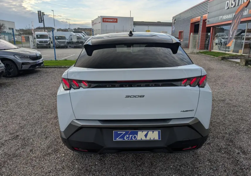 Vue arrière d'un Peugeot 3008 blanc hybride 2025 avec feux arrière à griffes LED et bandeau noir laqué entre les feux.