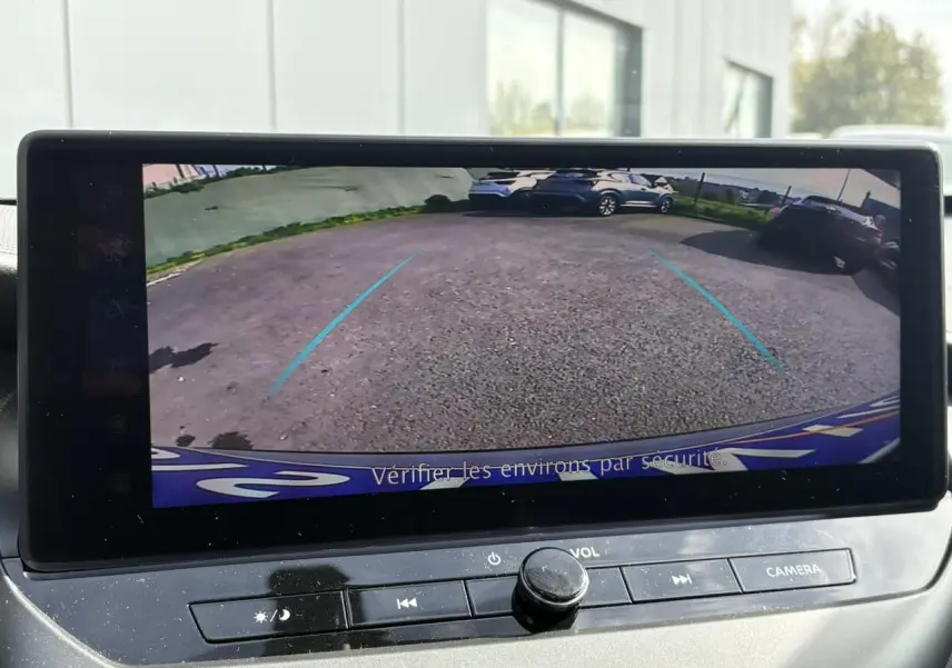 Vue de l'écran de caméra de recul affichant un parking avec plusieurs véhicules, dans un Nissan Juke gris Ceramic.