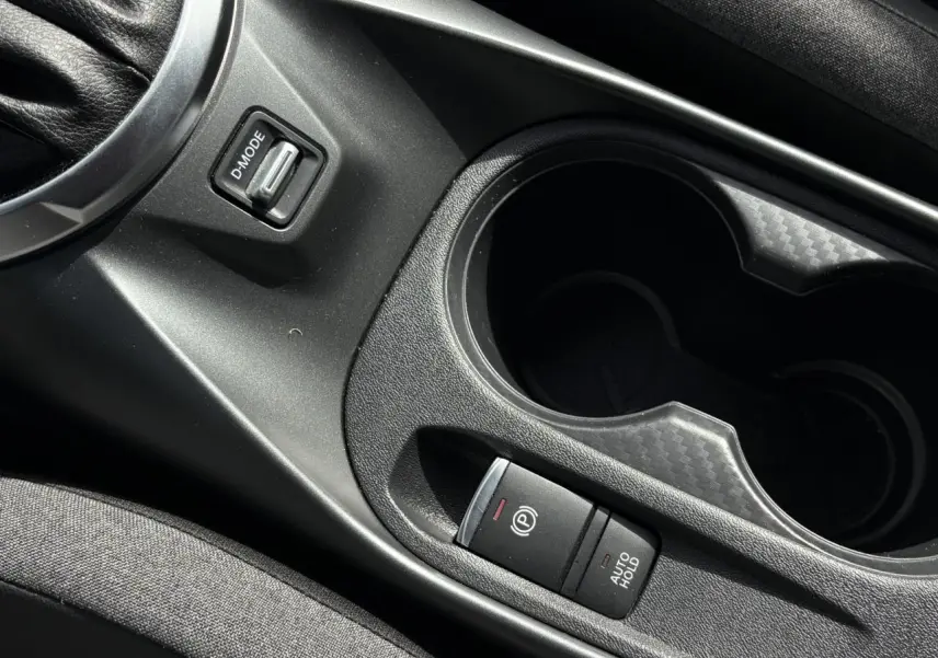 Gros plan sur la console centrale noire du Nissan Juke 2025, avec frein à main électrique et porte-gobelets.