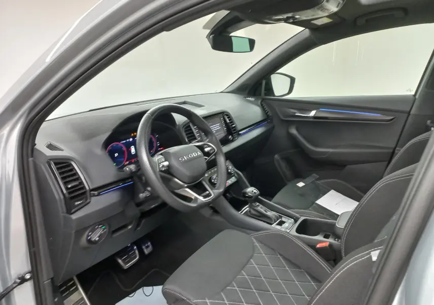 Intérieur avant droit du Skoda Karoq gris argent 2025, avec tableau de bord numérique et éclairage d’ambiance bleu.