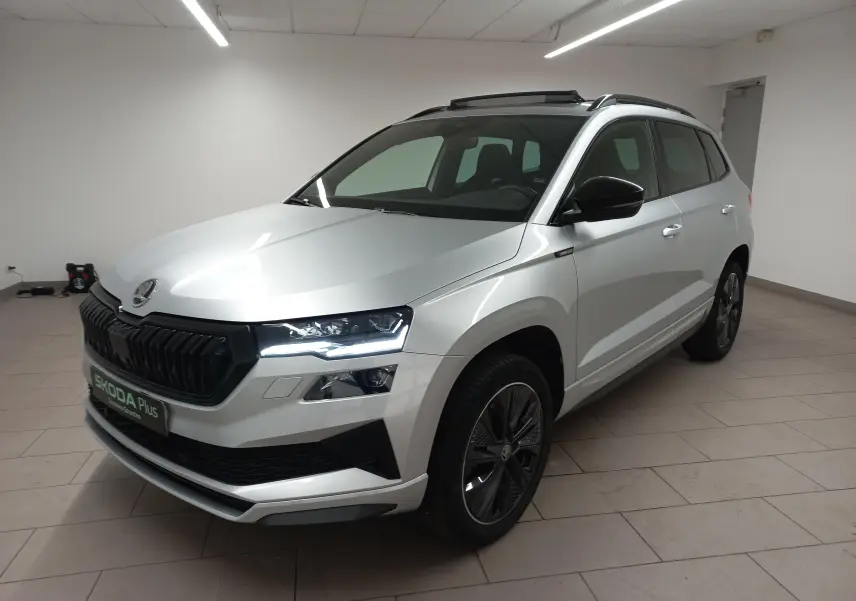 Vue 3/4 avant droite d'un Skoda Karoq gris argent avec toit panoramique ouvrant et jantes noires distinctives.