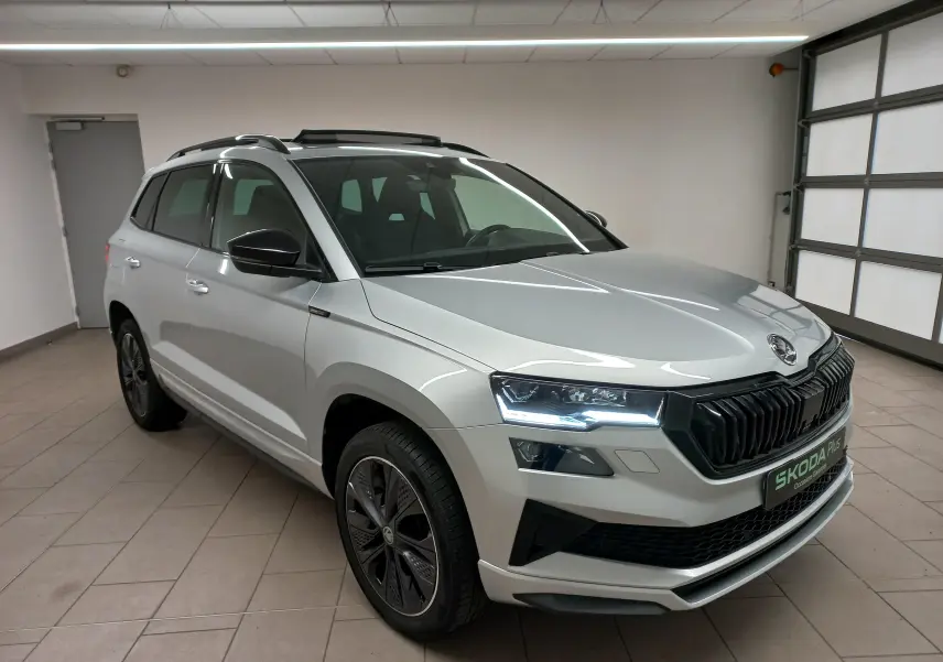 Vue 3/4 avant droite d’un Skoda Karoq gris argent avec toit panoramique ouvrant et calandre noire sportive.