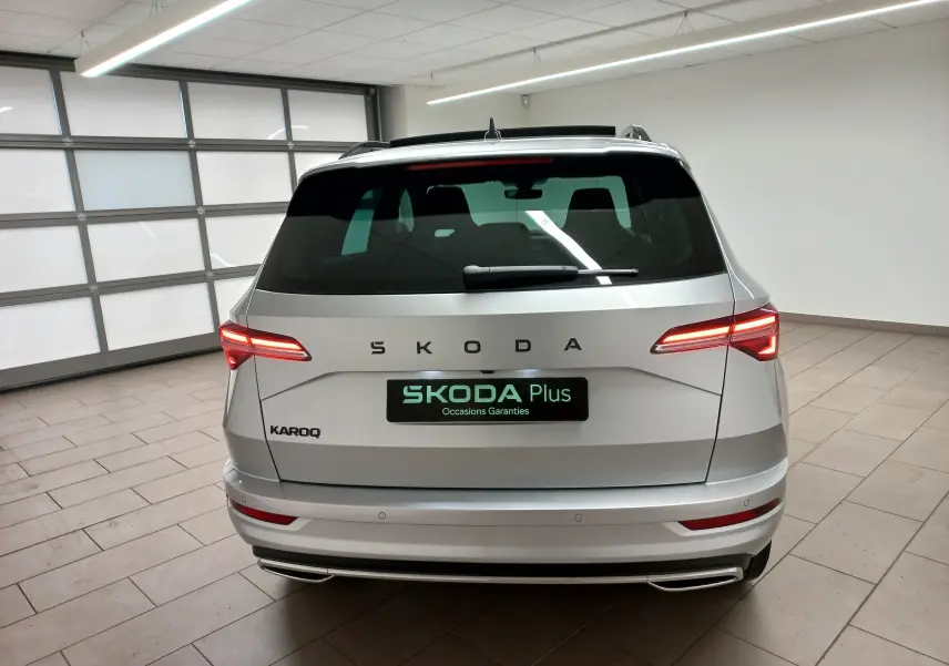 Vue arrière d'un Skoda Karoq gris argent 2025 avec feux allumés et hayon électrique dans un garage.