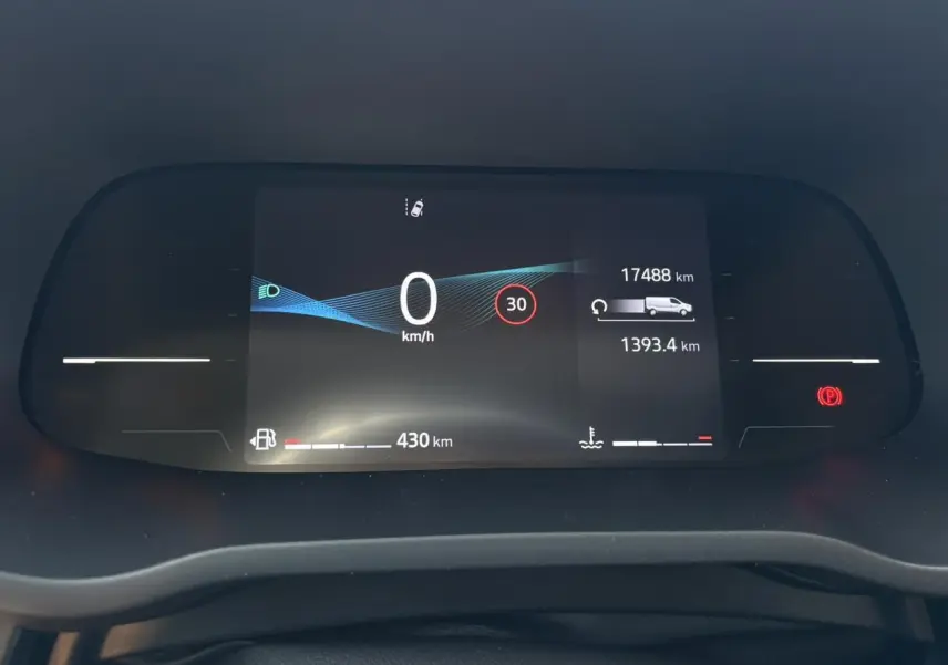 Tableau de bord numérique du Nissan Primastar Combi 2025 affichant vitesse, autonomie et alertes, vue frontale rapprochée.