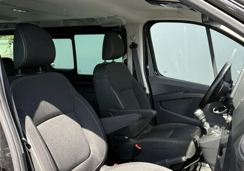 Vue intérieure côté conducteur du Nissan Primastar Combi noir Minuit, montrant sièges avant avec accoudoirs et levier de vitesse manuel.