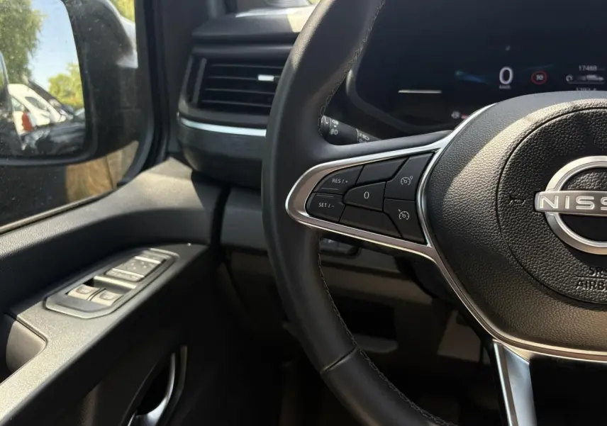 Vue intérieure côté conducteur du Nissan Primastar Combi 2025, volant multifonctions et commandes lève-vitres sur portière noire.
