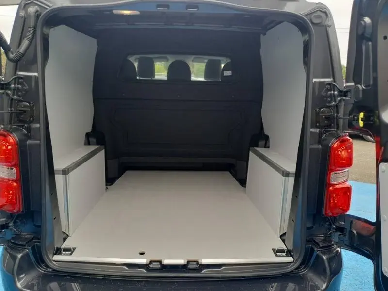 Vue arrière ouverte du Citroën Jumpy gris Titane métal, montrant l'espace de chargement aménagé avec cloison et rangements latéraux blancs.