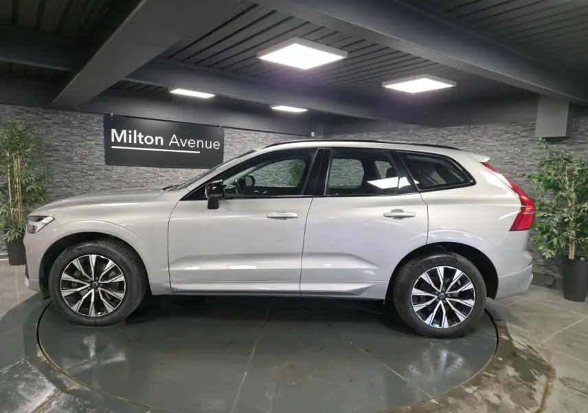 Volvo XC60 gris vue de profil côté gauche, avec jantes alliage noires et toit ouvrant panoramique visible.