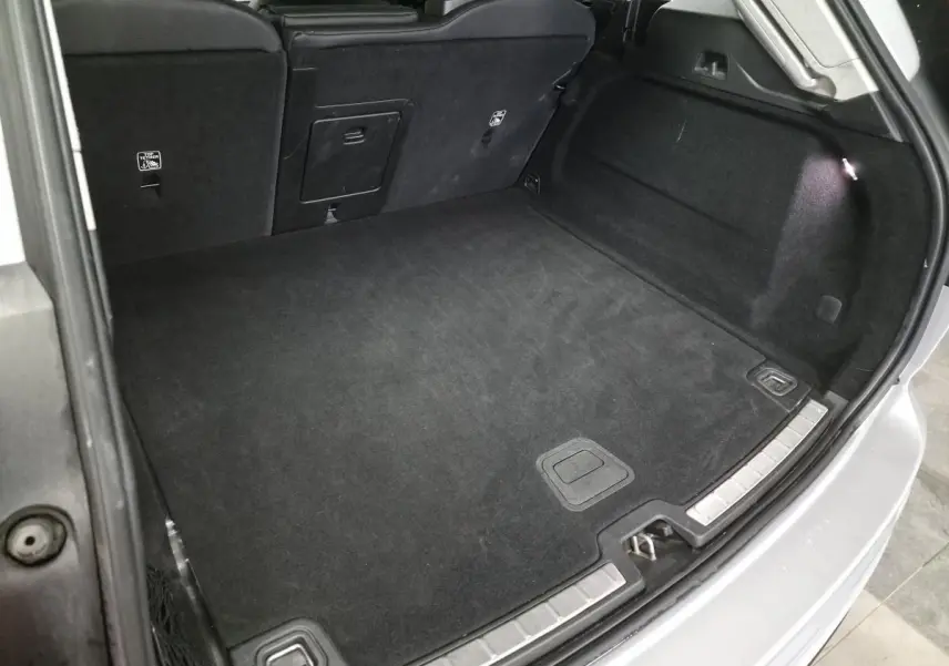 Coffre spacieux ouvert du Volvo XC60 gris 2023, avec tapis noir et éclairage intérieur visible.