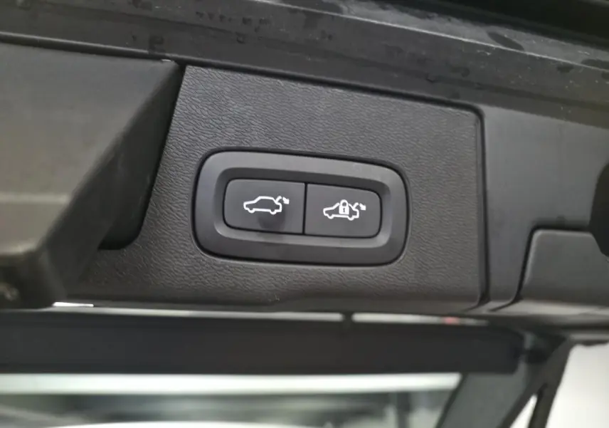Boutons d'ouverture et de verrouillage du hayon électrique sur le bord intérieur du coffre d'un Volvo XC60 gris.