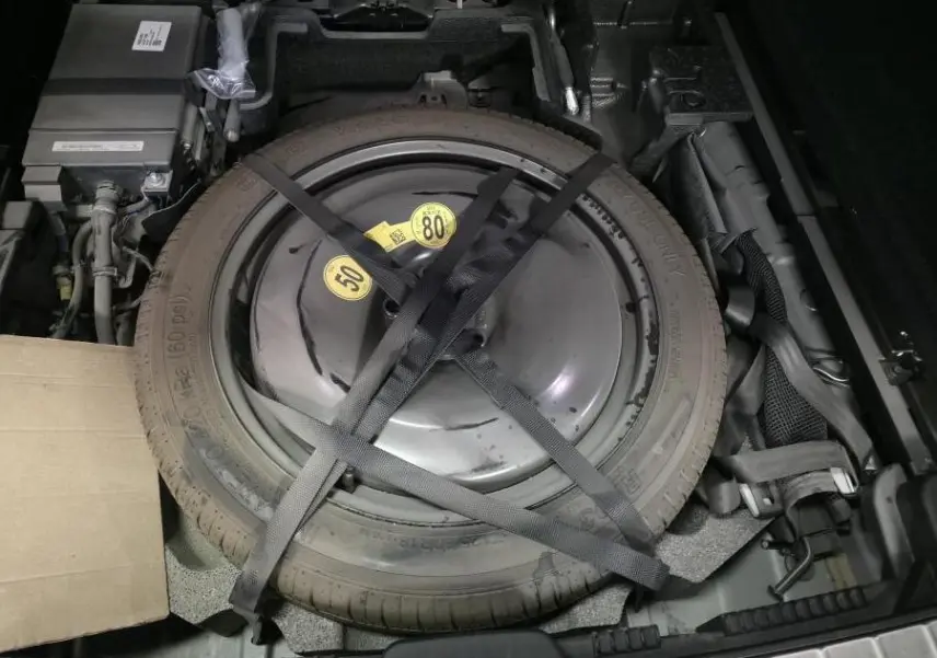 Vue plongeante sur la roue de secours temporaire grise fixée dans le coffre du Volvo XC60 gris 2023.