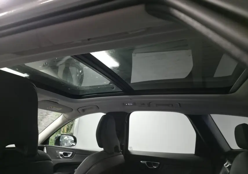 Vue intérieure du toit ouvrant panoramique en verre du Volvo XC60 gris, montrant les sièges avant et arrière noirs.