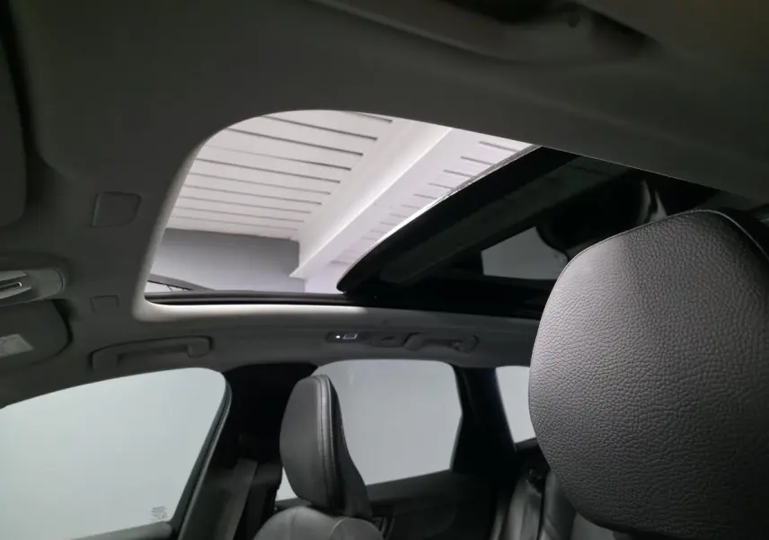 Vue intérieure du toit ouvrant panoramique ouvert et sièges avant en cuir noir du Volvo XC60 gris 2023.