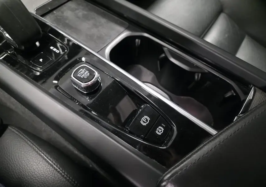 Gros plan sur la console centrale noire brillante du Volvo XC60 2023 avec bouton Start/Stop et commandes de frein à main.