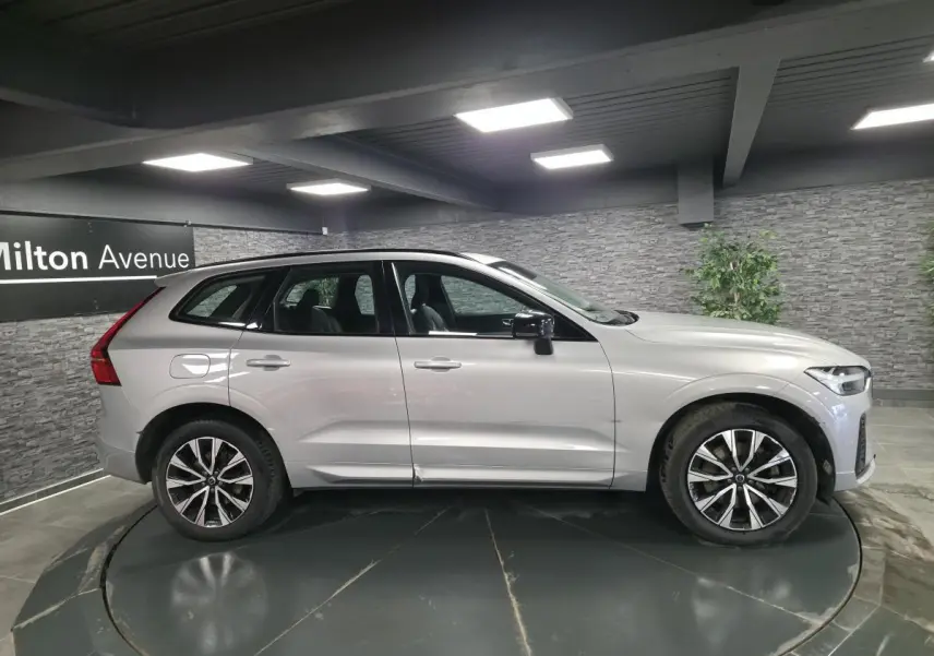 Vue latérale gauche d'un Volvo XC60 gris métallisé 2023 avec jantes alliage 19 pouces et toit ouvrant panoramique.
