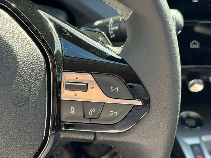 Gros plan sur les commandes multifonctions gauche du volant de la Peugeot 308 blanc Okénite, avec boutons volume et appel.