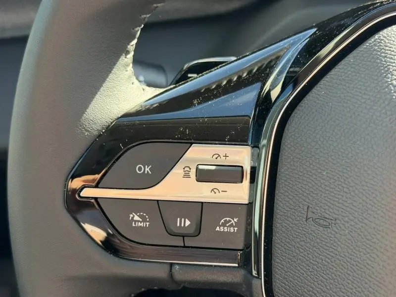 Gros plan sur les commandes multifonctions noires et argentées du volant de la Peugeot 308 hybride blanche.