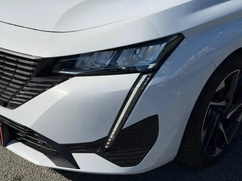 Gros plan sur l'avant droit blanc Okénite d'une Peugeot 308 2025, mettant en valeur le phare LED et la calandre noire.