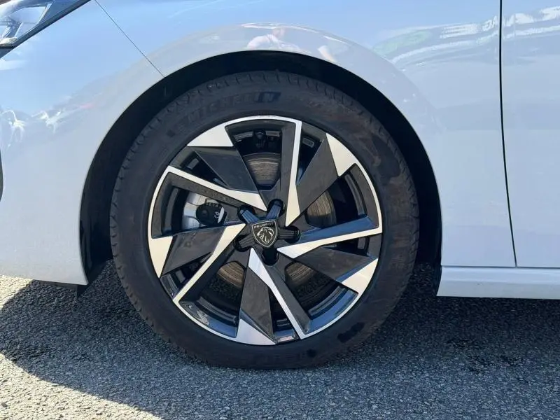Gros plan sur la jante alu noire et argentée de la roue avant droite d'une Peugeot 308 blanche Okénite.