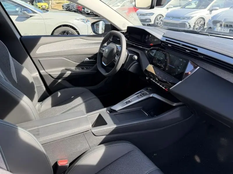 Vue intérieure côté conducteur de la Peugeot 308 Hybrid 2025, montrant le tableau de bord moderne et la console centrale noire.