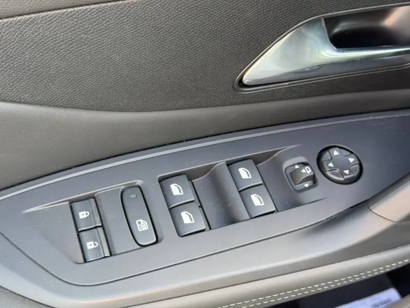 Vue rapprochée des commandes de lève-vitres et rétroviseurs côté conducteur de la Peugeot 308 blanche 2025.