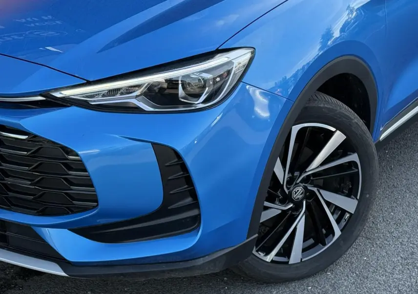 Gros plan sur l’avant droit bleu Como du MG ZS 1.5 Hybrid+ 197 Luxury avec phare LED et jante alliage 18 pouces.